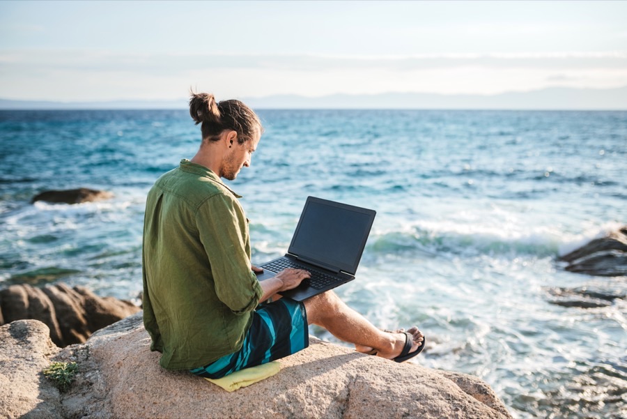 A U.S. expat working on a laptop at the edge of the ocean